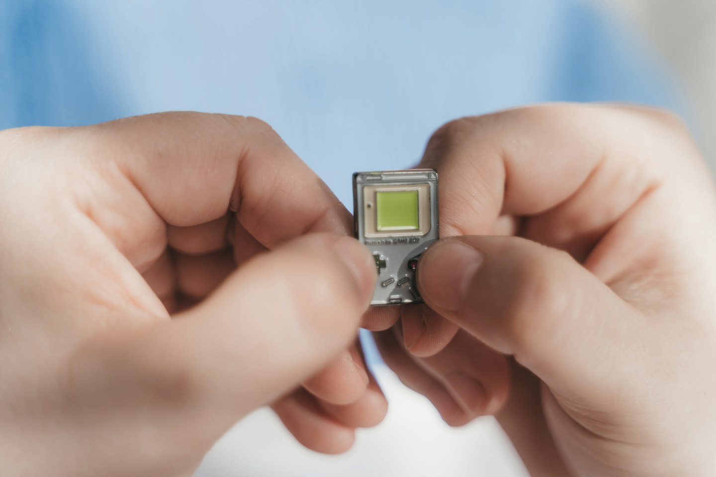Hands hold and operate a small silver retro game console.