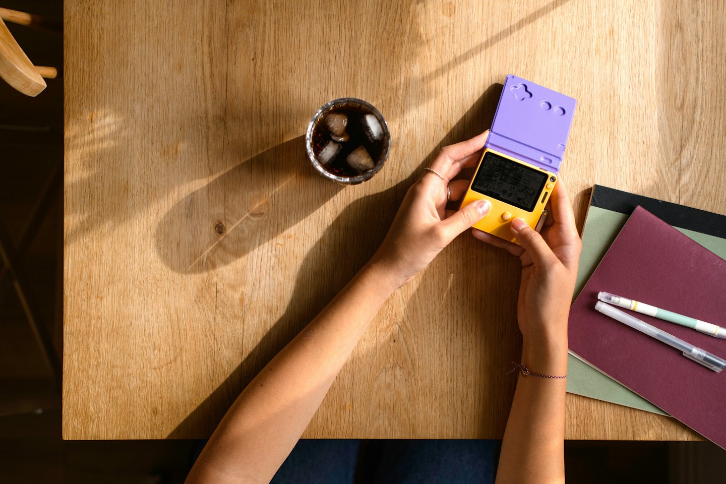 Hands holding an open yellow and purple handheld gaming device.