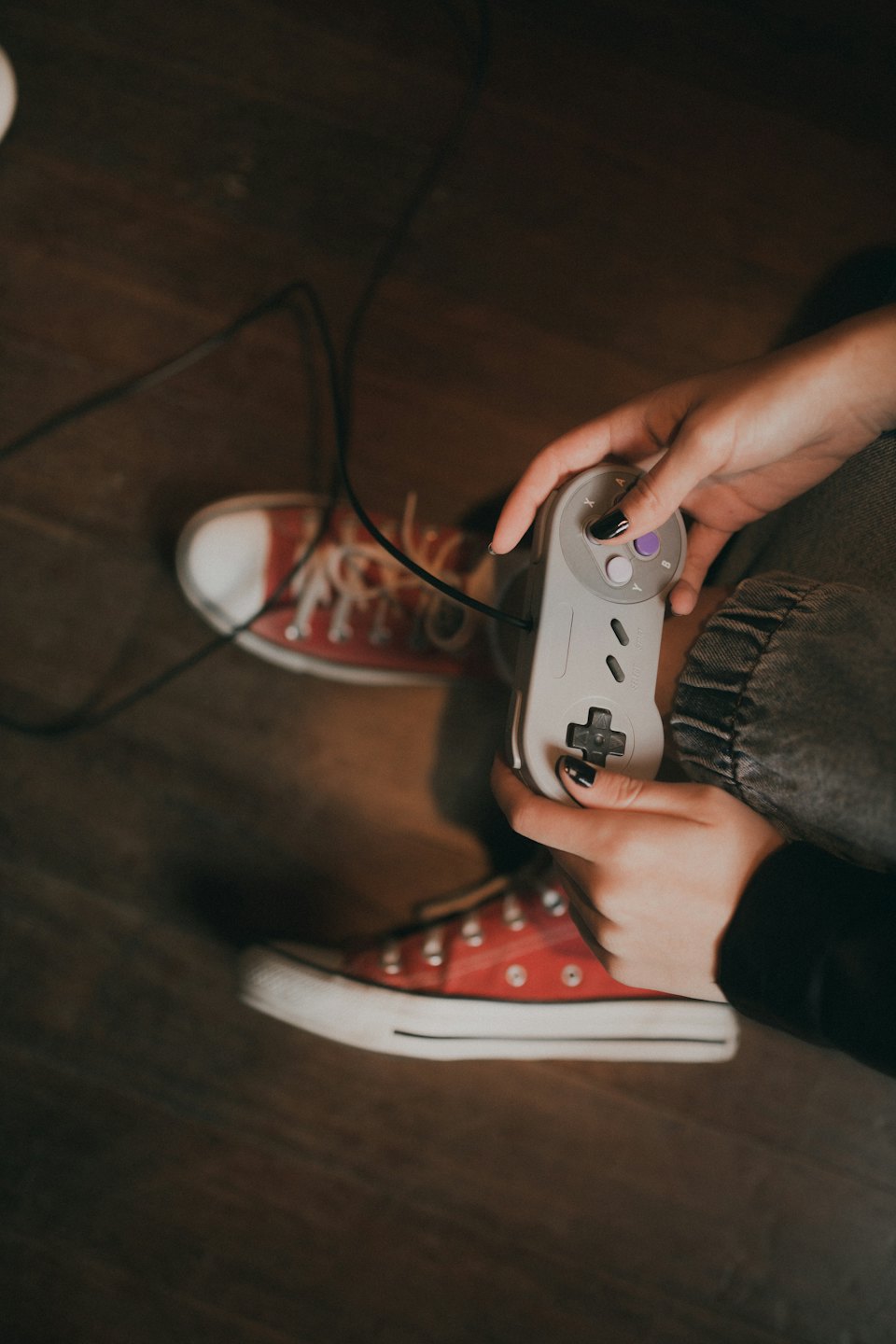 Person sits on a wooden floor holding a retro video game controller.