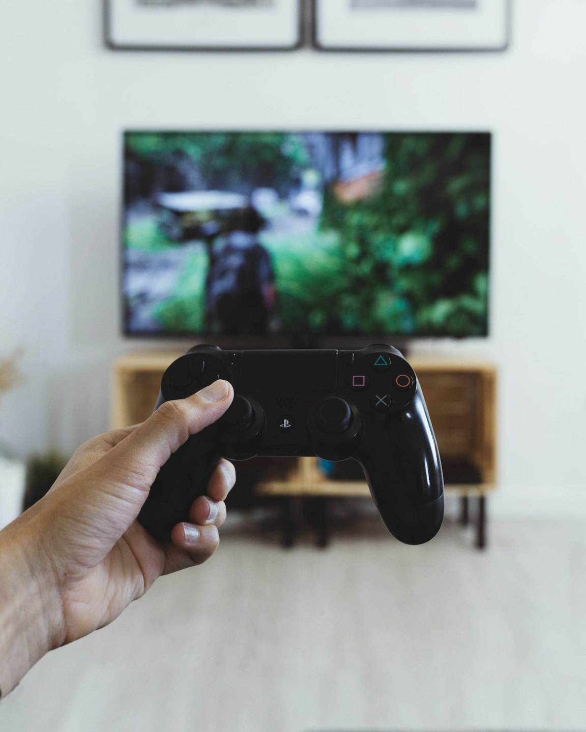 Hand holding a video game controller with a game on the TV.